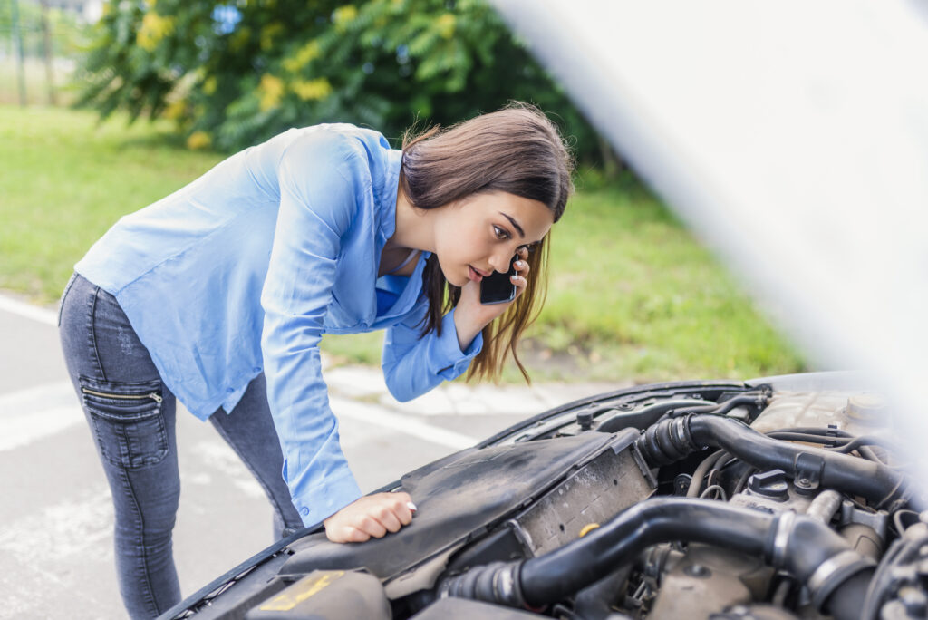 Mulher preocupada falando ao telefone enquanto verifica o motor do carro.