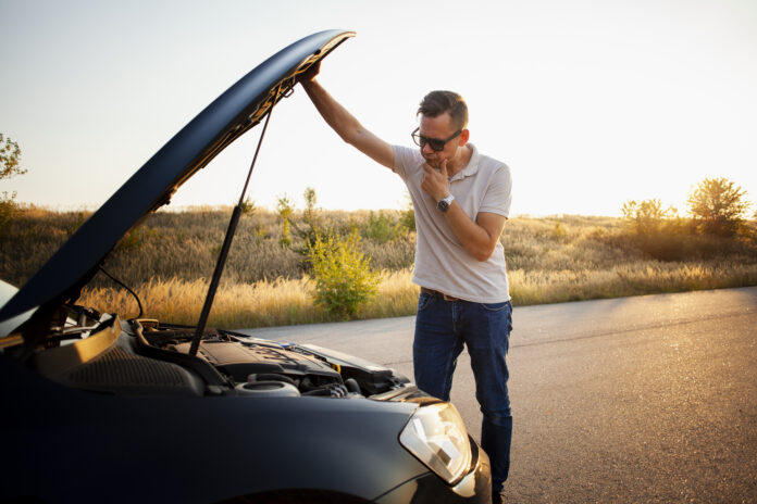 Homem verificando o motor do carro na estrada ao pôr do sol.