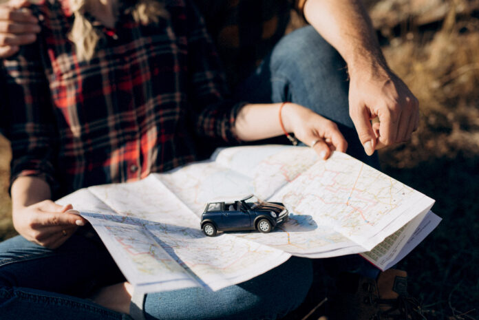 Mãos segurando um mapa com um carro em miniatura durante o planejamento de uma road trip