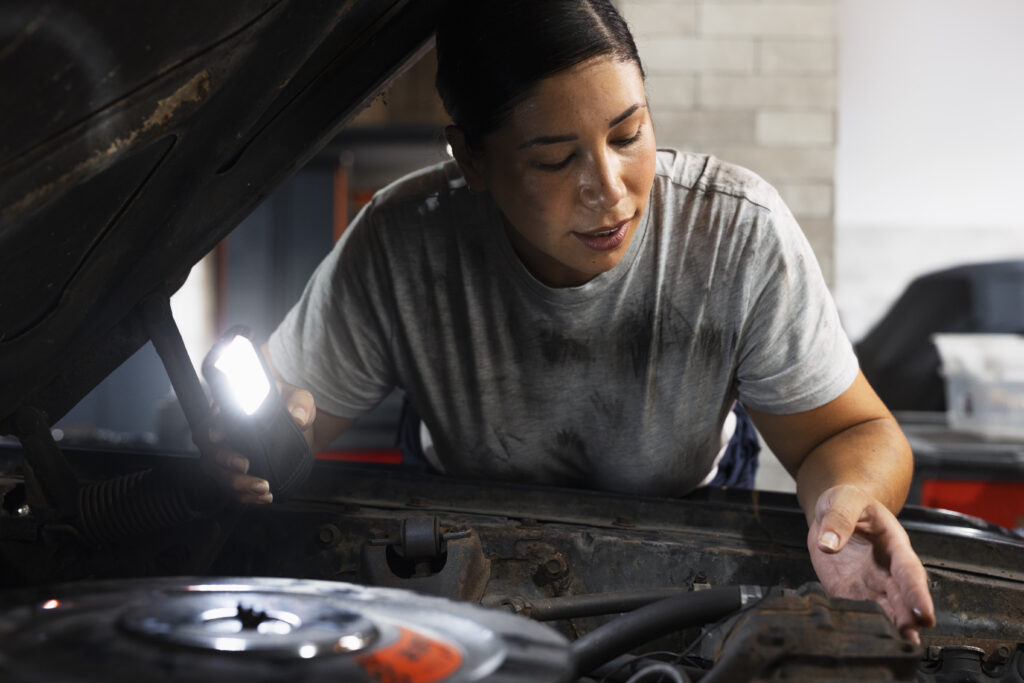 Mulher verificando motor do carro com uma lanterna para manutenção preventiva