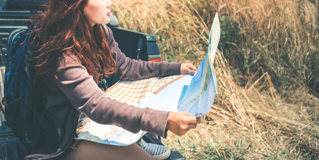 Mulher segurando um mapa sentada na traseira de um carro durante uma road trip