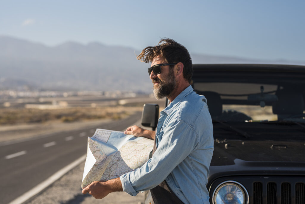 Homem segurando um mapa ao lado de um carro na estrada durante uma road trip