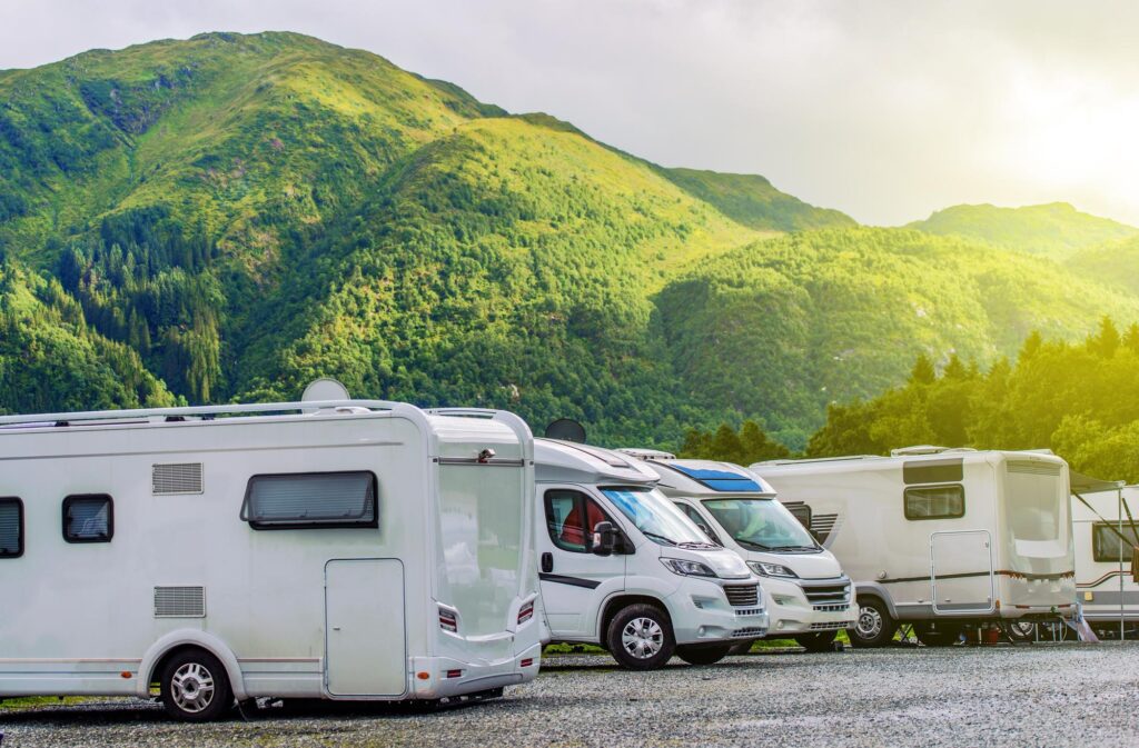 Vários motorhomes estacionados com montanhas verdes ao fundo, representando viagens ao ar livre e estilo de vida sobre rodas.