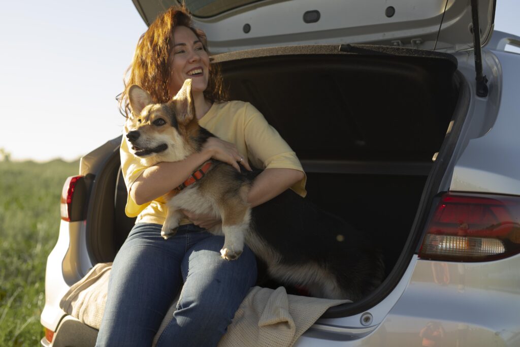 Mulher sorrindo enquanto segura um cachorro no porta-malas aberto do carro, durante uma viagem ao ar livre.