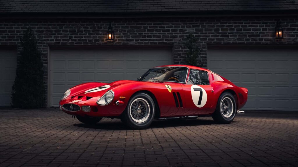 Ferrari 250 GTO vermelha, considerada um dos carros mais raros e valiosos do mundo, estacionada em frente a uma garagem.